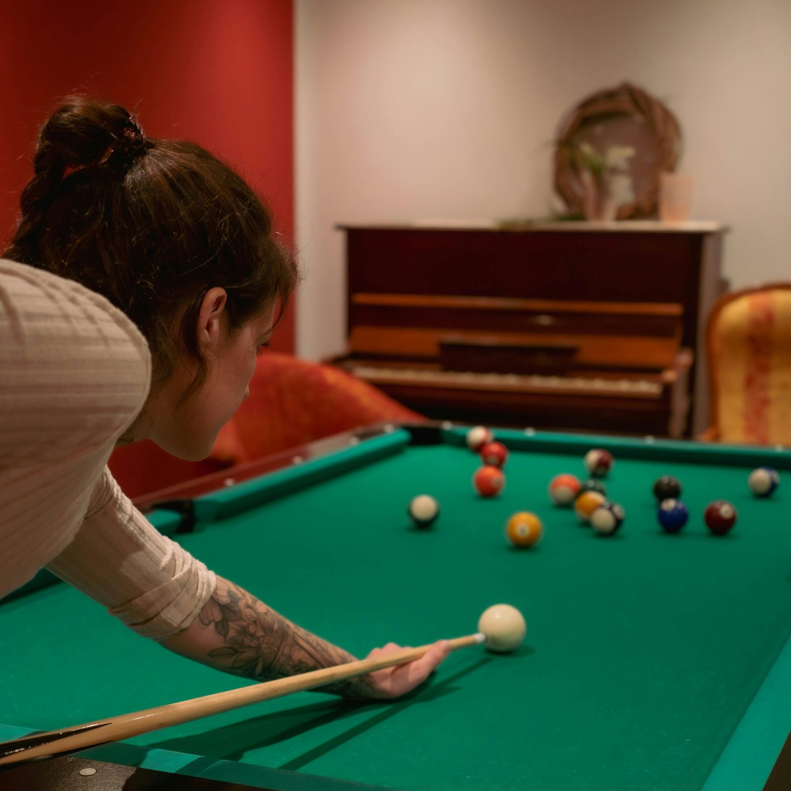 A woman skillfully playing billiards in a cozy indoor setting with a piano in the background.