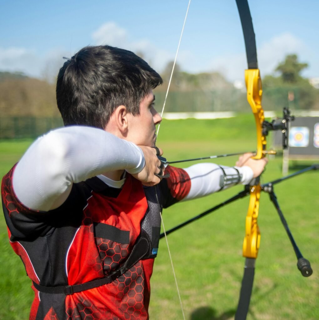 An archer aiming a bow at targets in an outdoor field on a sunny day.