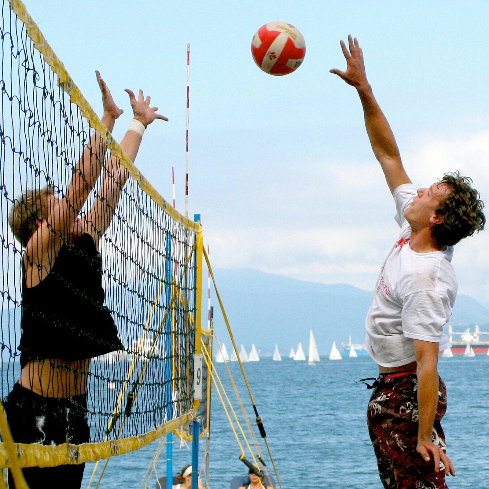 Two men engaged in a beach volleyball match near the ocean with blue skies.