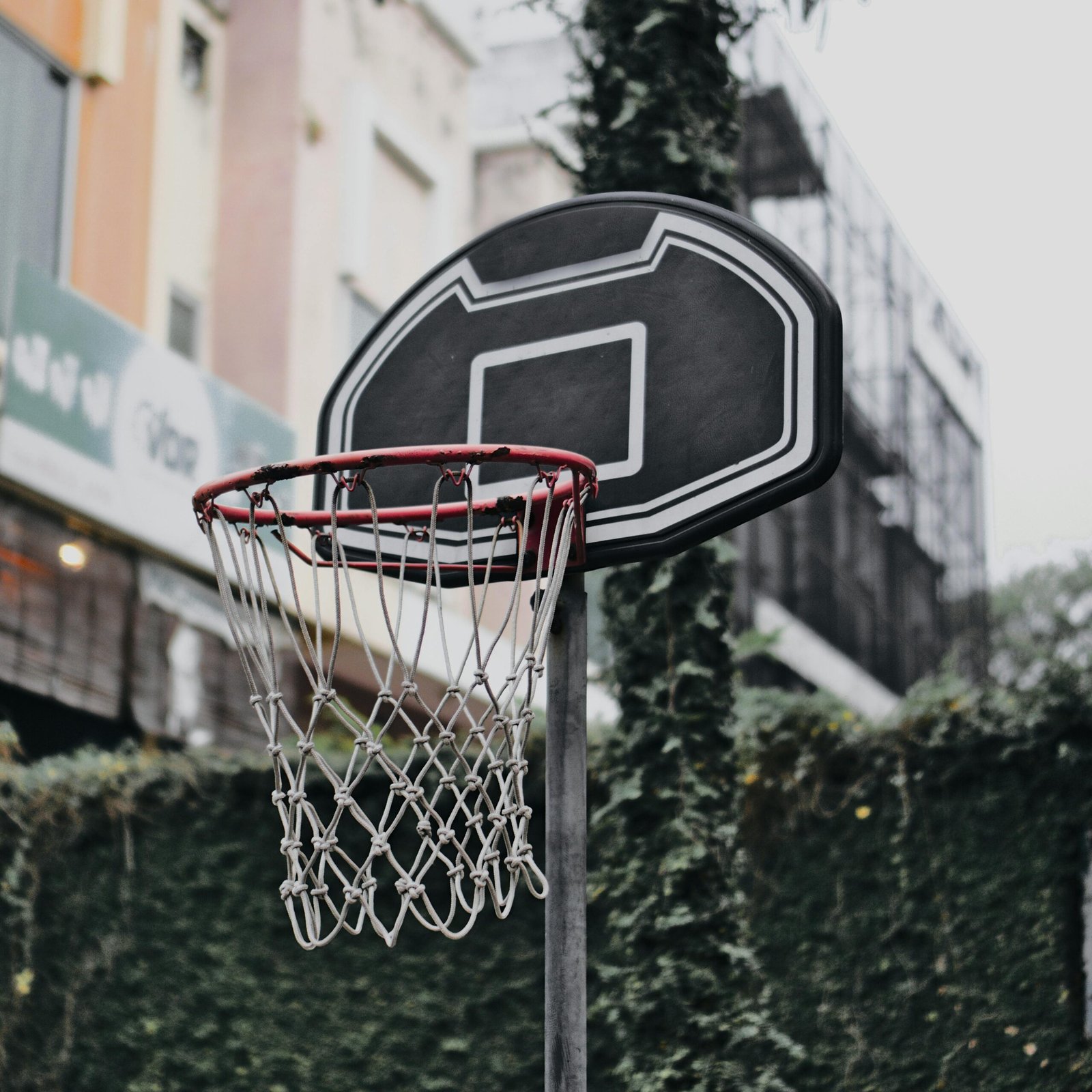 Close-up of a black outdoor basketball hoop with net against an urban backdrop, ideal for sports imagery.