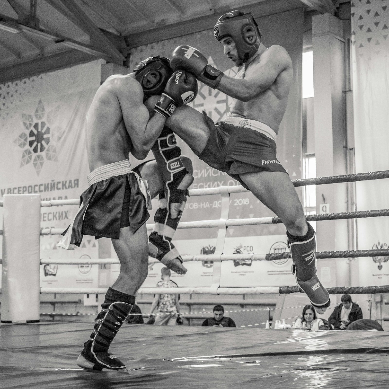 Intense black and white action shot of kickboxers in a competitive match.